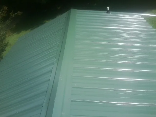 New green metal panels meeting at the ridge of a roof — Flat Roof Repair work by our crew in Springville