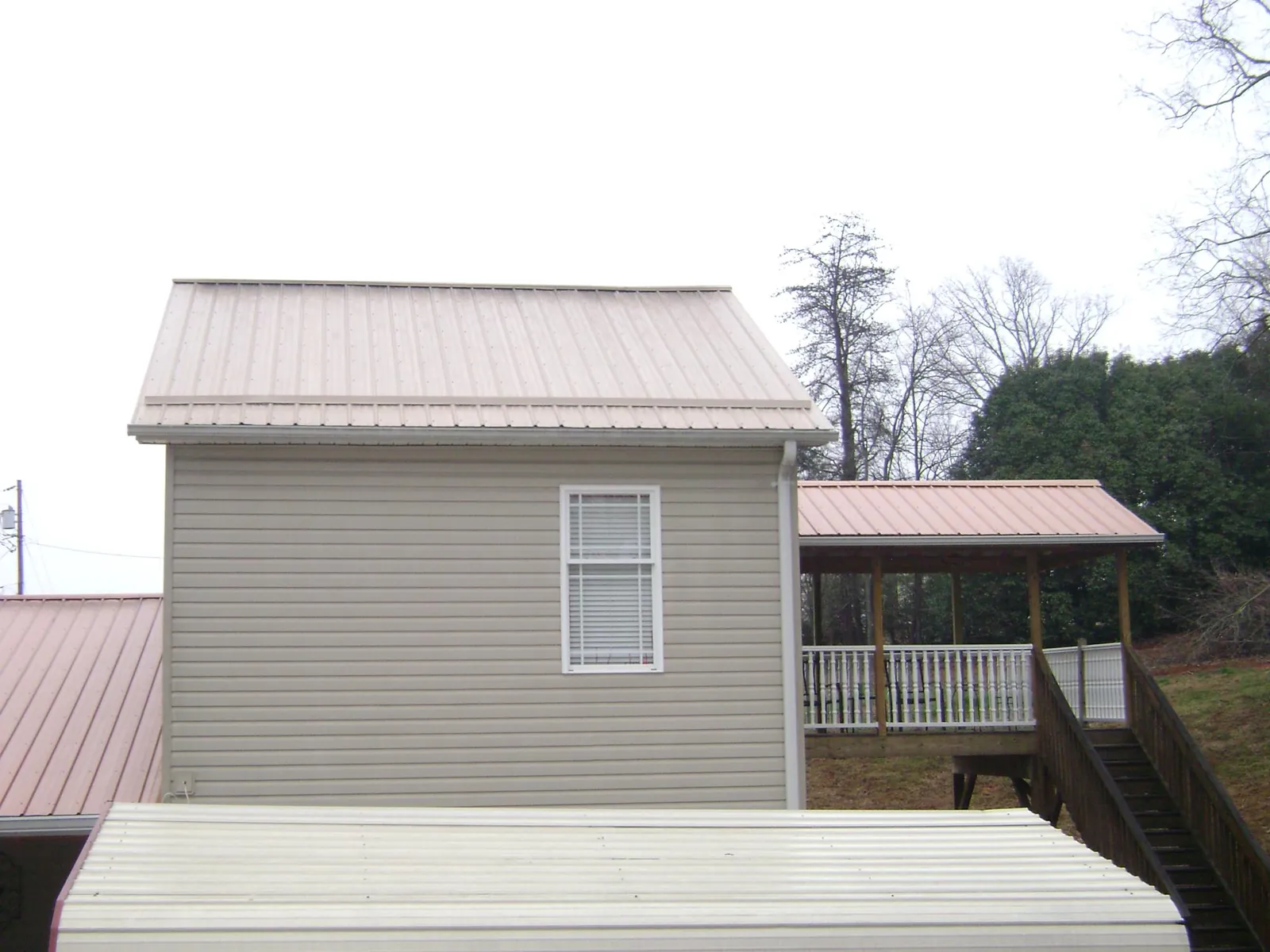 Tan metal roofs on a two story addition and attached porch, from a Roof Replacement job in Springville